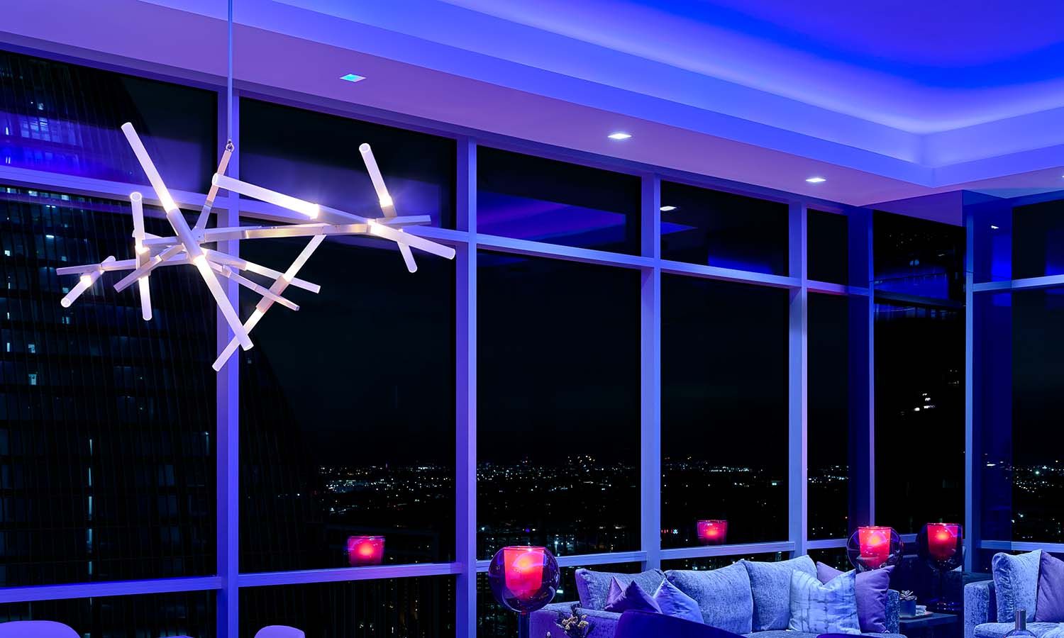 Living room at night with blue ambient lighting and city view through large windows