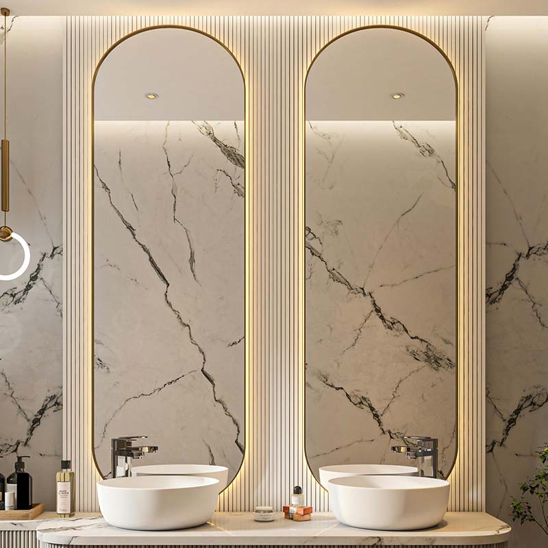 Arched mirror with built-in LED illumination above dual sinks, set against a marble backdrop.
